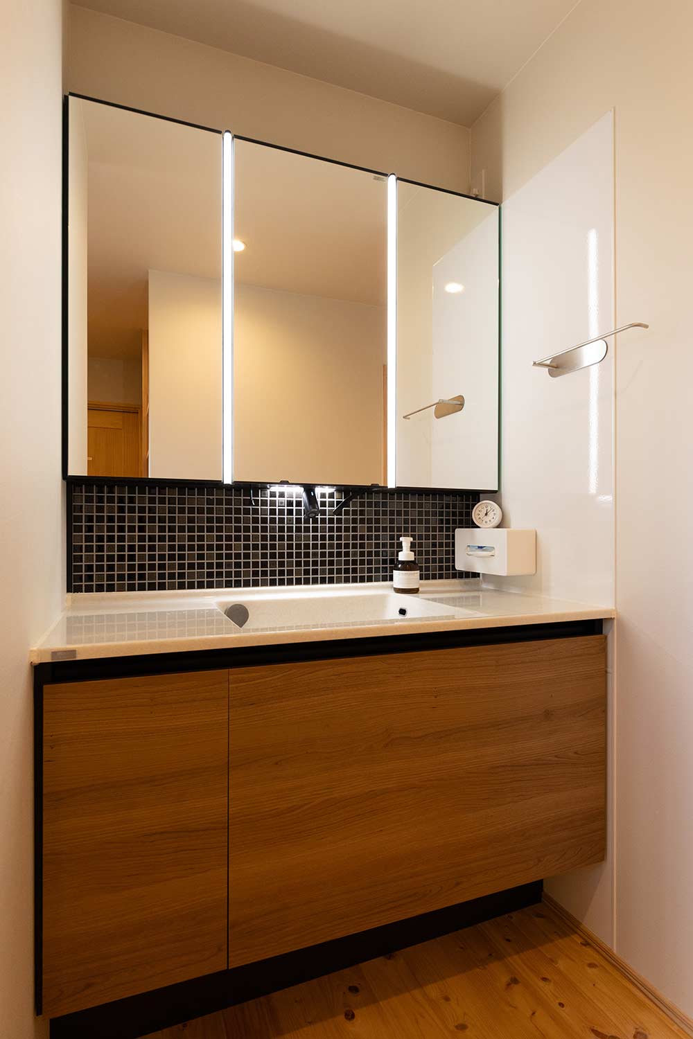 木目調のキャビネットにブラックのタイルで引き締め、デザイン性と機能性を両立した洗面スペース
